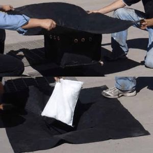 Two people are covering a fire pit with a black blanket, possibly for safety or to extinguish the flames.